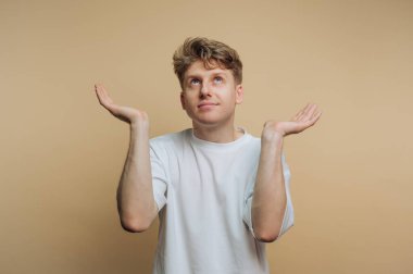 Kolları havada ve avuçları havada bir adam ayakta duruyor. Stüdyoda poz verirken kafasını kaldırıyor. Arka plan yumuşak, sade bir renk onu öne çıkarıyor..