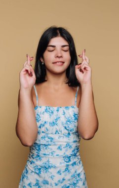 Genç bir kadın arka planda gözleri kapalı duruyor. Umut işareti olarak parmaklarını çapraz yapar. Onun kıyafeti mavi çiçekli bir elbise. Odaklanmış görünüyor..