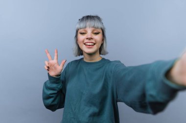 Genç bir kadın gün boyunca açık renkli bir odada kendi portresini çekerken elini kaldırarak gülümsüyor ve poz veriyor..