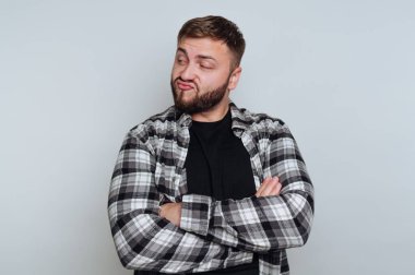 Çapraz kollar ve neşeli bir ifadeyle duran bir adam. Onun kısa saçı ve sakalı var. Arka plan aydınlık, kareli bir gömlek ve siyah bir tişört giyiyor..