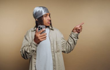 Sade bir geçmişi olan genç bir adam stüdyoda duruyor. Bir elinde akıllı telefon, diğer elinde de işaret ediyor. Saçları örülmüş ve başörtüsüyle kaplanmış..