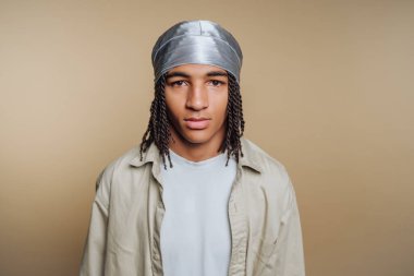 Genç bir insan doğrudan kameraya bakarak duruyor. Gümüş bir başörtüsü ve açık renk bir üst giyiyorlar. Arkaplan sade ve tarafsız, ifadelerine ve tarzlarına odaklanmış..