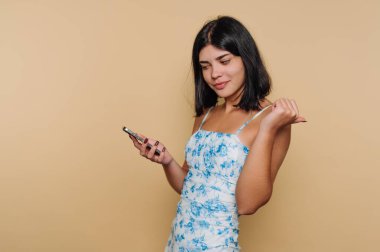 Genç bir kadın düz bir duvarın önünde duruyor, akıllı telefonuna bakıyor. Zamanını iyi geçiriyor ve muhtemelen mesajları okuyor. Onun günlük kıyafetleri sahnenin rahatlatıcı havasına katkı sağlıyor..