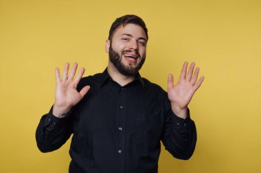 Siyah tişörtlü, gülümseyen adam ellerini sarı arka plana kaldırdı..