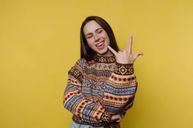 Renkli kazaklı kadın sarı arka planda kaya jesti yapıyor..