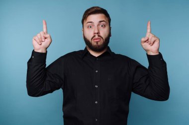 Siyah gömlekli adam şaşırmış bir ifadeyle yukarı bakıyor.