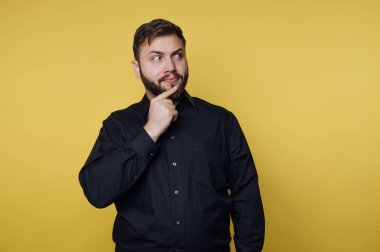 Siyah gömlekli adam sarı arka planı düşünüyor.