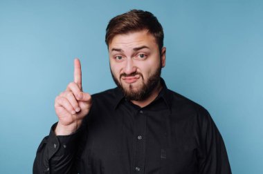 Siyah gömlekli adam mavi arka plana karşı uygunsuz bir hareket yapıyor..