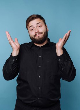 Siyah gömlekli adam mavi arka plana karşı omuz silkiyor..