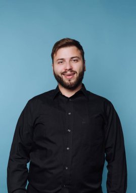 Mavi arka planda siyah gömlekli, gülümseyen adam..