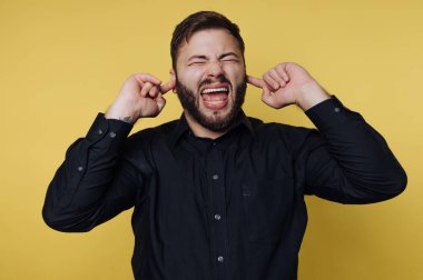 Siyah gömlekli, kulakları sarı arka planda olan bir adam..