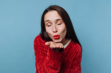 Kırmızı süveter giymiş bir kadın mavi arka planda öpüşüyor..