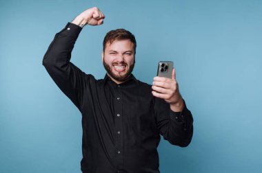 Siyah gömlekli adam akıllı telefona bakarken kutlama yapıyor..