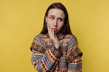 Sarı arka plandan endişe eden desenli kazaklı bir kadın..