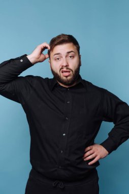 Siyah gömlekli bir adam kafası karışık bir şekilde kaşınıyor.