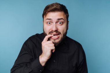 Sakallı ve bıyıklı bir adam parmağını ısırıyor, endişeli görünüyor..