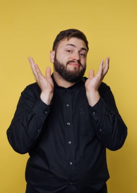 Siyah gömlekli adam sarı arka plana karşı omuz silkiyor..