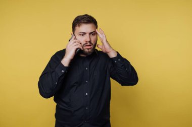 Siyah gömlekli bir adam telefonda şaşkın bir ifadeyle konuşuyor.