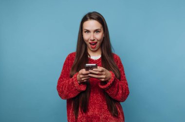 Kırmızı kazaklı kadın akıllı telefon kullanırken şaşırmış görünüyor..