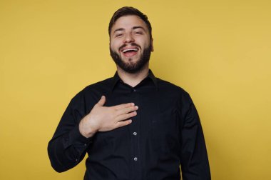 Siyah gömlekli adam sarı arka plana gülüyor.