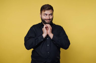 Siyah tişörtlü, sarı arka planda yaramaz bir yüz ifadesi olan adam..