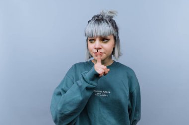 Gri saçlı kadın, gri arkaplana karşı şşşş hareketi yapıyor..