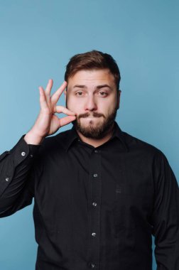 Siyah gömlekli adam mavi arkaplana karşı jest yapıyor.