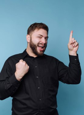 Siyah gömlekli adam yumruğunu sallayarak ve yukarı kaldırarak kutluyor.