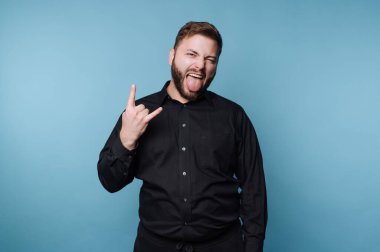 Siyah gömlekli adam kaya gibi el hareketi yapıyor ve dilini dışarı çıkarıyor..