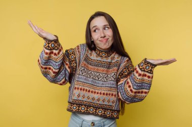 Renkli kazaklı bir kadın sarı arka planda omuz silkiyor..