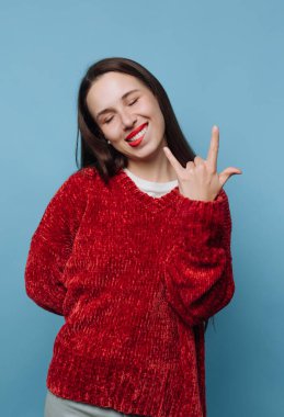 Kırmızı kazaklı bir kadın mavi arka planda rock 'n roll hareketi yapıyor..