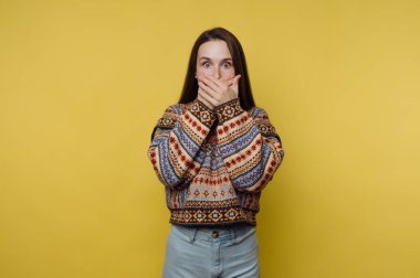 Şaşırmış bir kadın ellerini sarı arka planda tutarak ağzını kapatıyor..