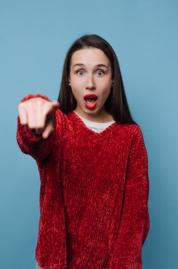 Kırmızı kazaklı kadın mavi arka planda kameraya bakıyor..