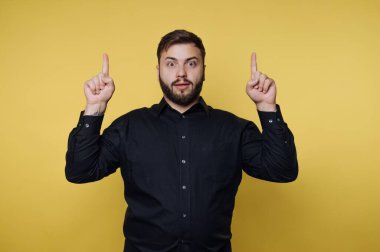 Siyah gömlekli adam sarı arkaplanı işaret ediyor..