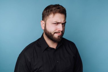 Mavi arka plana karşı şüpheci bir ifadeye sahip bir adam..