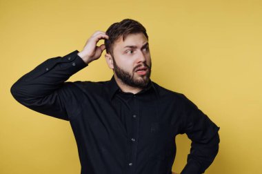 Siyah gömlekli bir adam sarı arka planda kafasını kaşıyor..