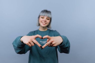 Gülümseyen kişi, mavi arka planda elleri olan kalp şekli yaratıyor..