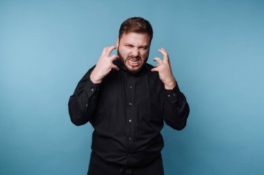 Siyah gömlekli bir adam mavi arka plana karşı öfkesini ifade ediyor..