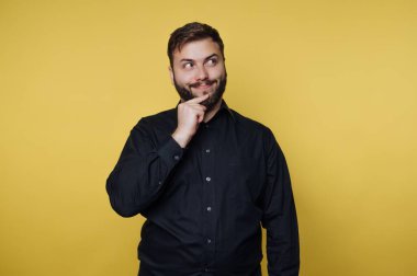 Siyah gömlekli adam sarı arka planı düşünüyor.