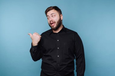 Siyah gömlekli bir adam mavi arka planda başparmağıyla hareket ediyor..