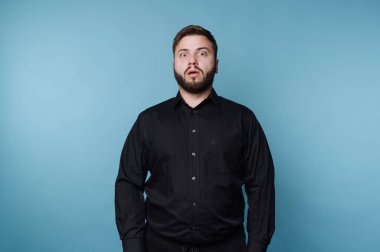 Siyah gömlekli adam mavi arka planda şaşırmış bir ifade var..