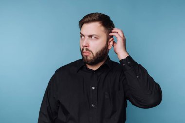 Siyah gömlekli bir adam kafasını mavi arka plana sürtüyor.