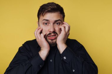 Siyah gömlekli bir adam sarı arka planda endişeli görünür..