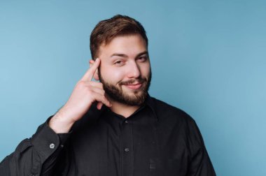 Siyah gömlekli adam mavi arka planda düşünme hareketi yapıyor..