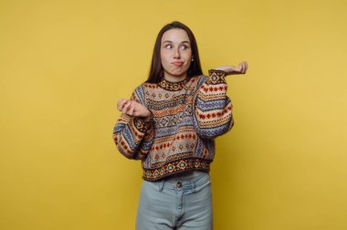 Renkli kazaklı bir kadın sarı bir arka plana karşı karışık bir ifade takınıyor..