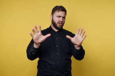 Siyah gömlekli adam sarı arka planda duruyor..