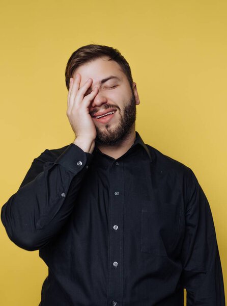 Man in black shirt laughing with hand on face against yellow background.