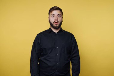 Sarı arka planda siyah gömlekli, şaşırmış bir adam..