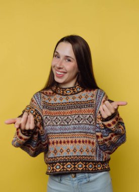 Sarı arka planda beliren, desenli süveterli, gülümseyen kadın.