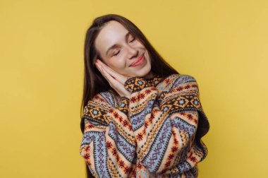 Sarı arka planda poz veren rahat kazaklı, gülümseyen kadın..